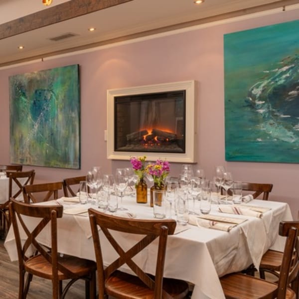 A dining room with a long table set for dinner, featuring a fireplace and abstract art.