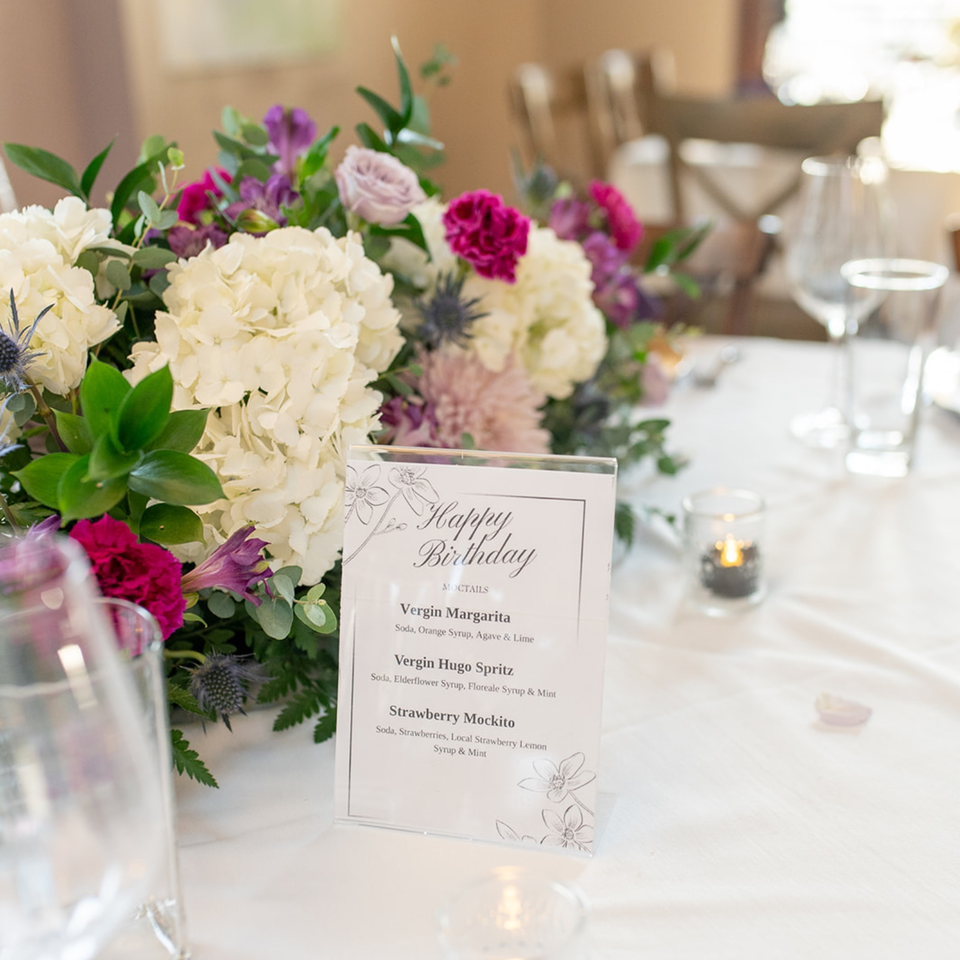 Floral centerpiece and birthday mocktail menu displayed on an elegantly set restaurant table.