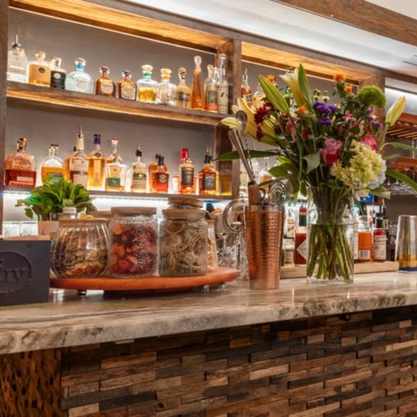 A well-stocked bar with liquor bottles on shelves, a floral arrangement, and cocktail ingredients.