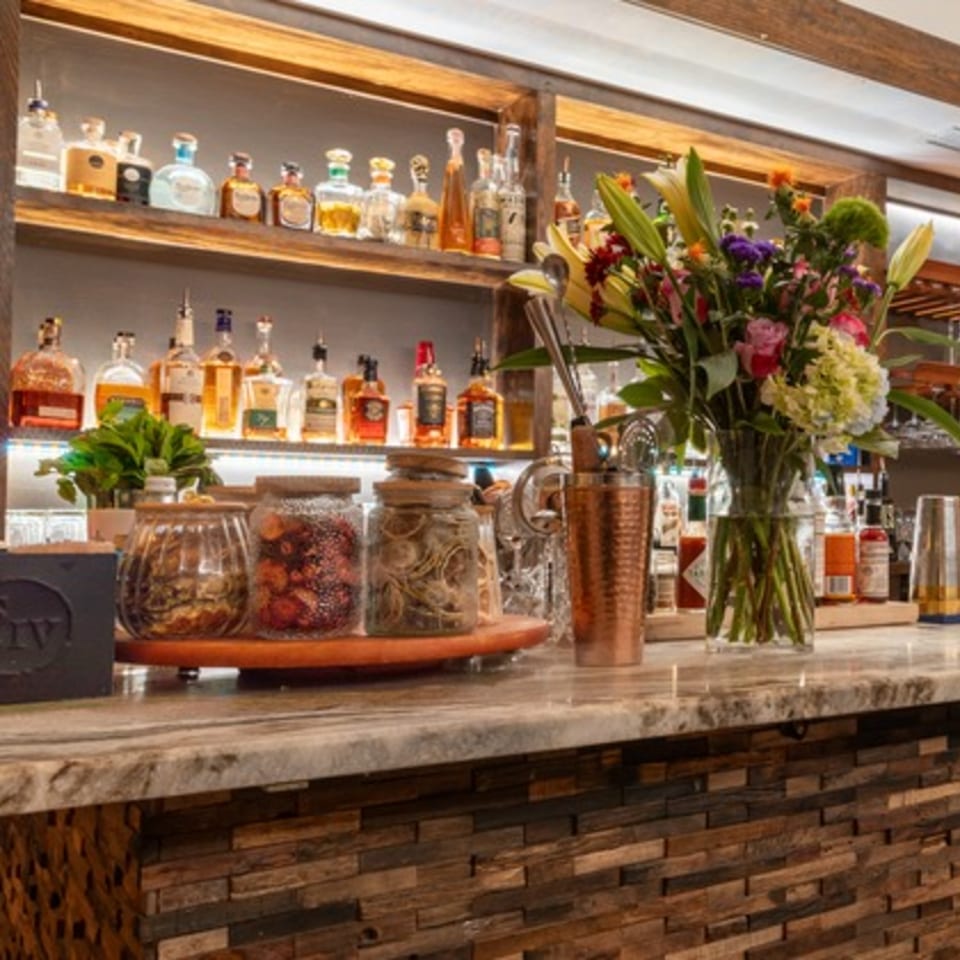 A well-stocked bar with liquor bottles on shelves, a floral arrangement, and cocktail ingredients.