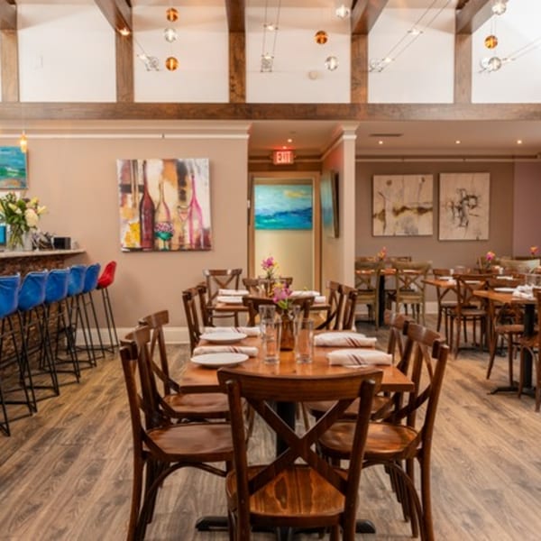 Restaurant dining room with wooden tables and chairs, a bar with blue stools, and abstract art.