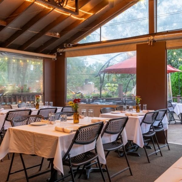 An outdoor dining area with white-clothed tables, black chairs, and string lights, overlooking a patio.
