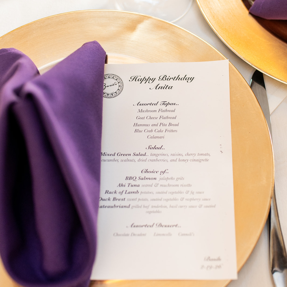 Birthday dinner menu for Anita rests on a gold charger plate beside purple napkins and tableware.
