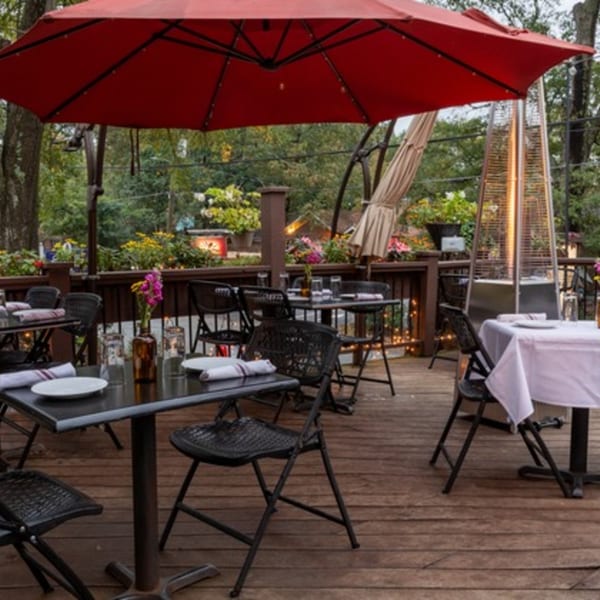 Outdoor restaurant patio with black tables and chairs, red umbrellas, and a patio heater.