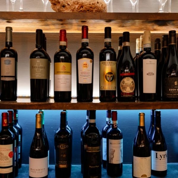 Two wooden shelves filled with various wine bottles, some with red and gold labels, against a blue light.