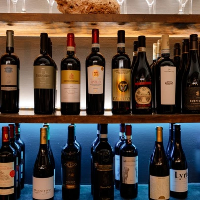 Two wooden shelves filled with various wine bottles, some with red and gold labels, against a blue light.